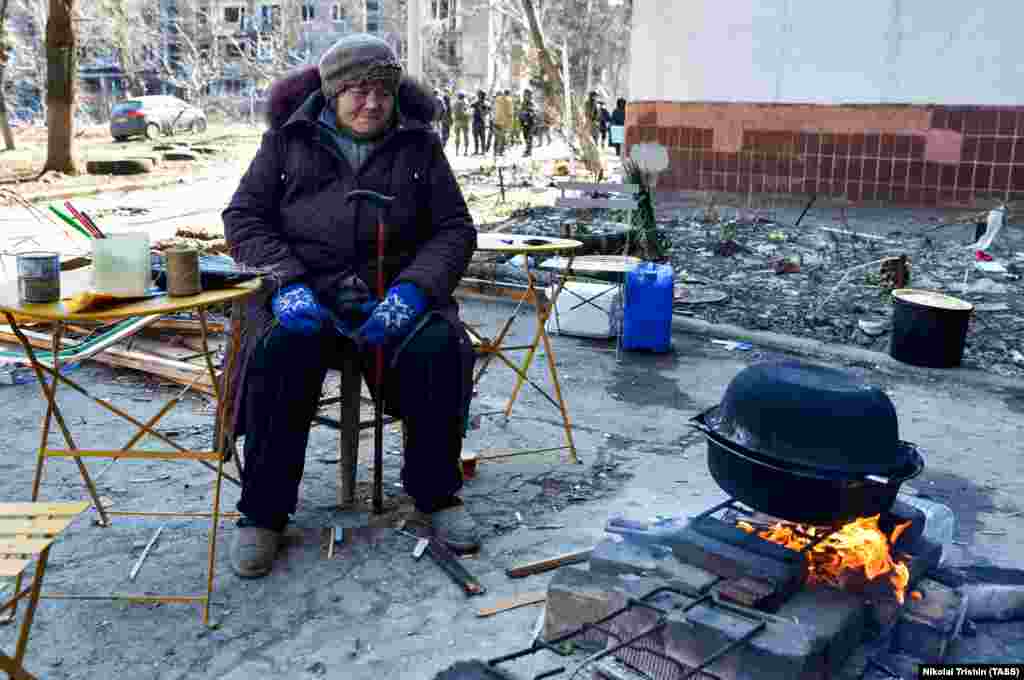 Женщина готовит еду на открытом огне в жилом квартале, поврежденном российскими обстрелами. Люди пытаются растопить снег, чтобы получить питьевую воду. Мариуполь, 19 марта 2022 года