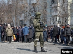 Солдат російської армії стоїть біля місцевих жителів в Маріуполі, березень 2022 рік