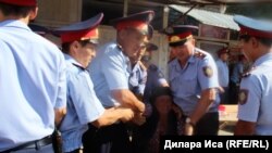 Полиция қызметкерлері орталық базарда дүңгіршектерін сүруге қарсылық танытқан саудагерді ұстап әкетіп барады. Шымкент, 30 шілде 2018 жыл.